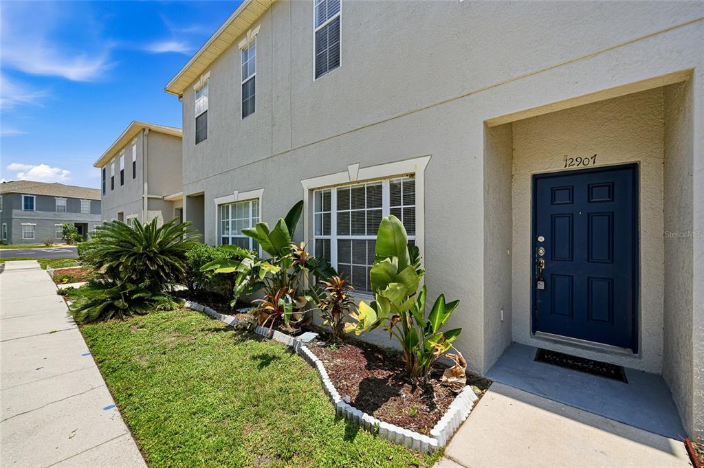 A two-story beige townhouse exterior features a blue front door and a small garden bed — 12907 KINGS CROSSING DRIVE, GIBSONTON, FL