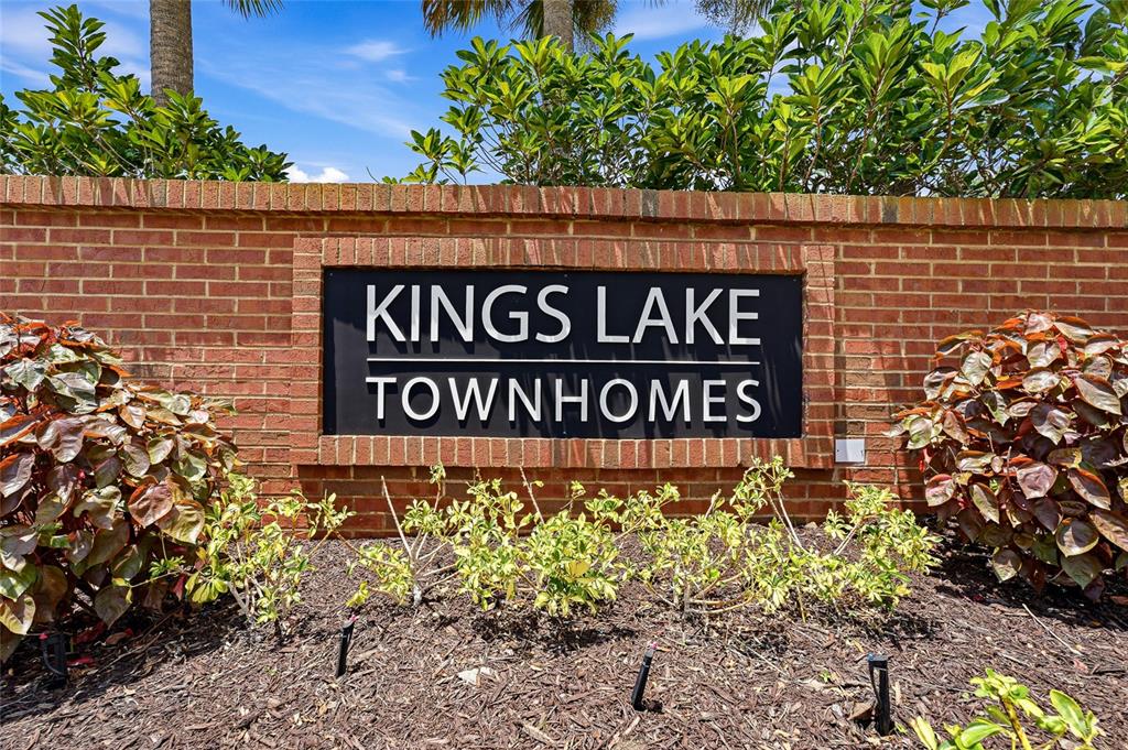 A brick wall features a black sign reading Kings Lake Townhomes surrounded by landscaping — 12907 KINGS CROSSING DRIVE, GIBSONTON, FL