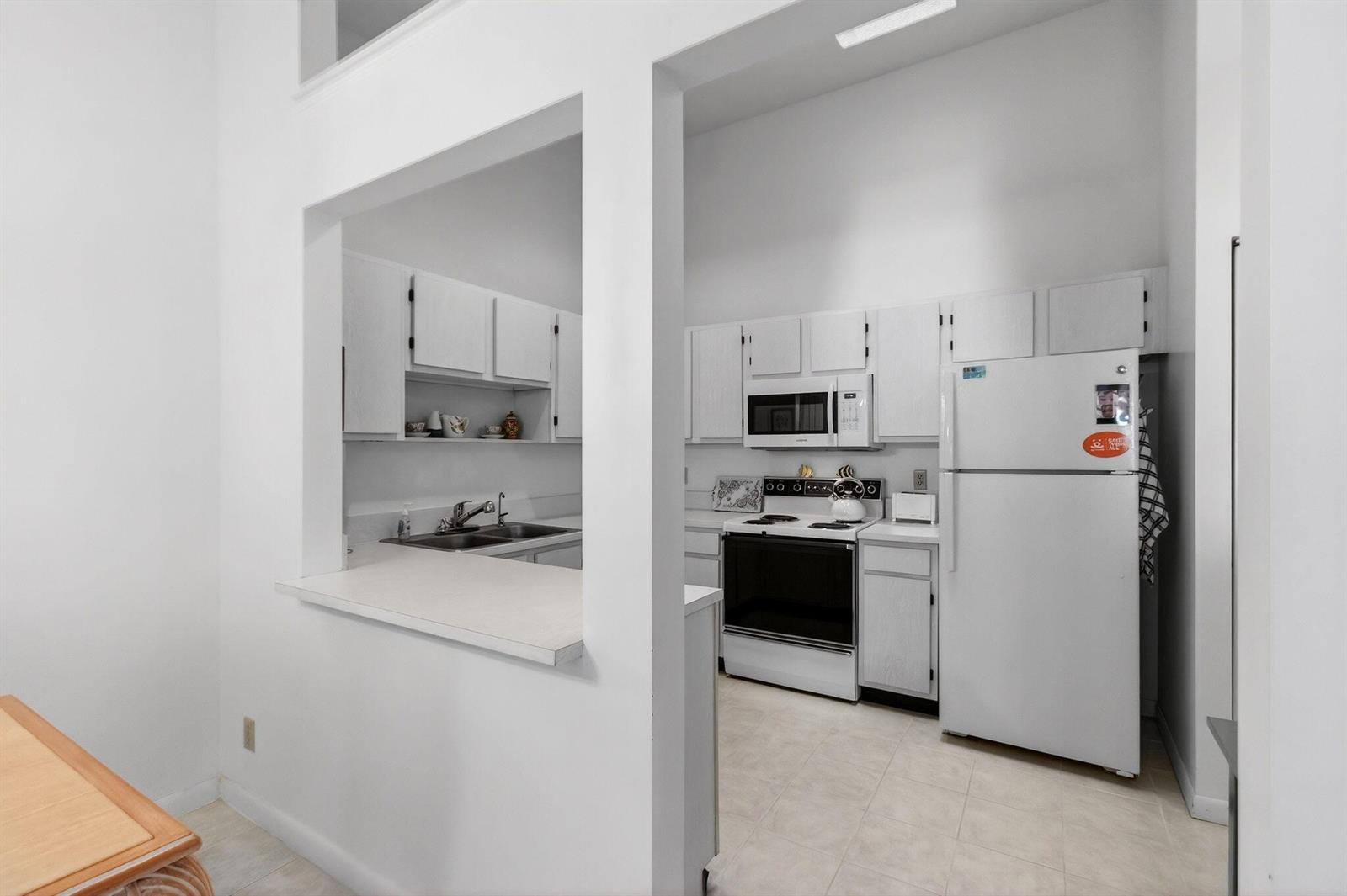 A white kitchen with a pass-through window, white appliances, and light-colored tile flooring — 3814 Coco Loba Lane, Boynton Beach FL 33436, BOYNTON BEACH, FL
