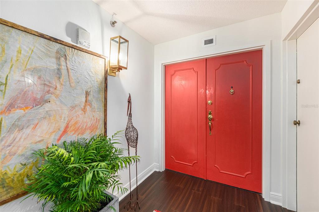 An entryway features a bright red double door, dark wood flooring, and a large bird painting — 3301 BAYSHORE BOULEVARD UNIT 1601E, TAMPA, FL