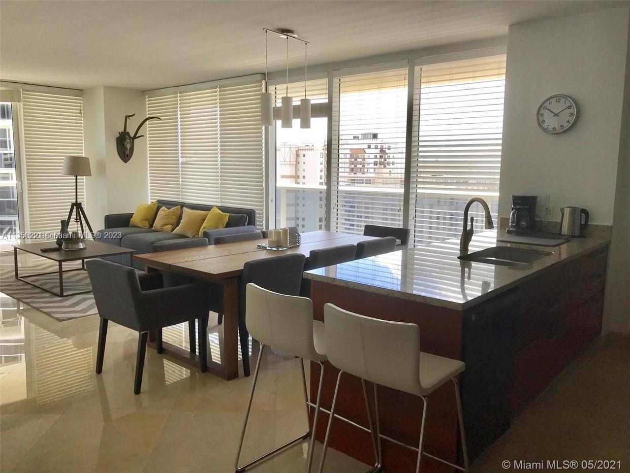 An open-concept living and dining area features a kitchen island, wooden table, and floor-to-ceiling windows — 1830 S Ocean Dr # 1706, Hallandale Beach FL 33009, HALLANDALE BEACH, FL