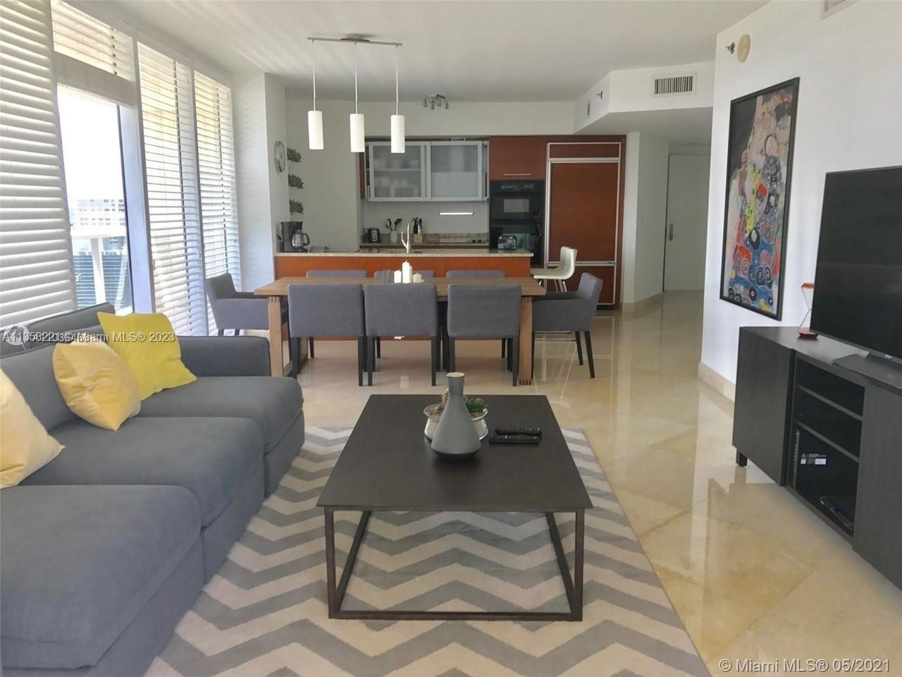 A modern living and dining area features a grey sofa, wooden table, and open kitchen — 1830 S Ocean Dr # 1706, Hallandale Beach FL 33009, HALLANDALE BEACH, FL