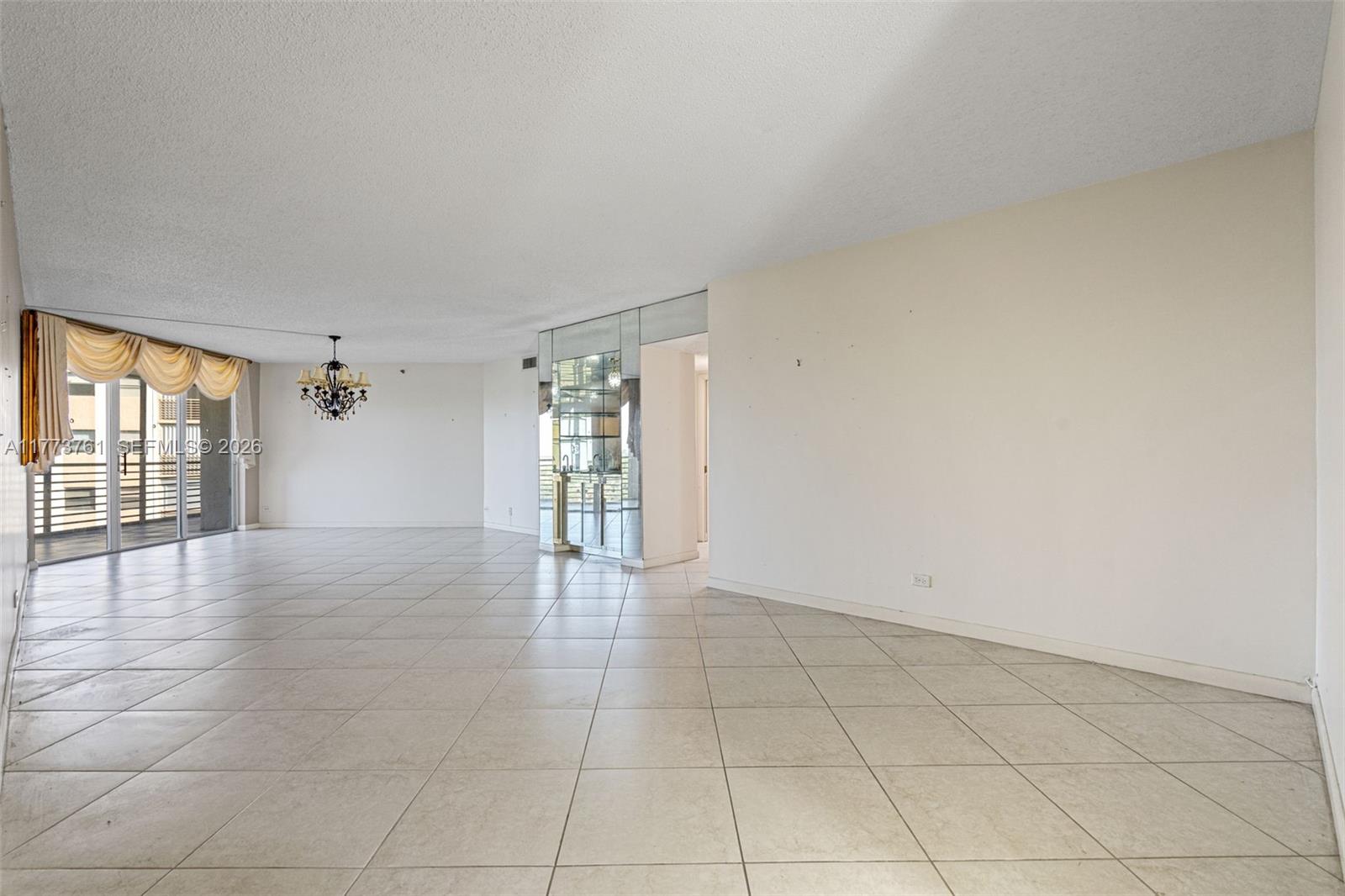 A spacious, empty living room features large light-colored floor tiles and a mirrored wet bar — 7200 Radice Ct # 709, Lauderhill FL 33319, LAUDERHILL, FL
