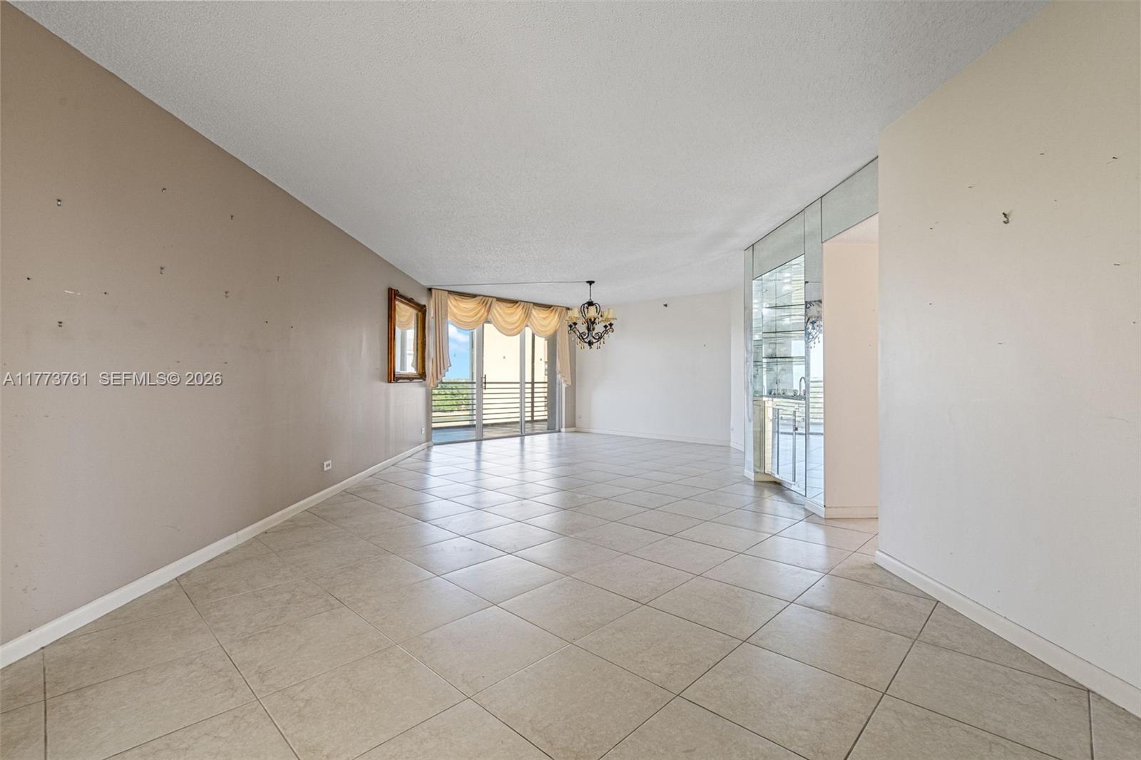 An empty living room features beige tile flooring, a mirrored wet bar, and a balcony — 7200 Radice Ct # 709, Lauderhill FL 33319, LAUDERHILL, FL