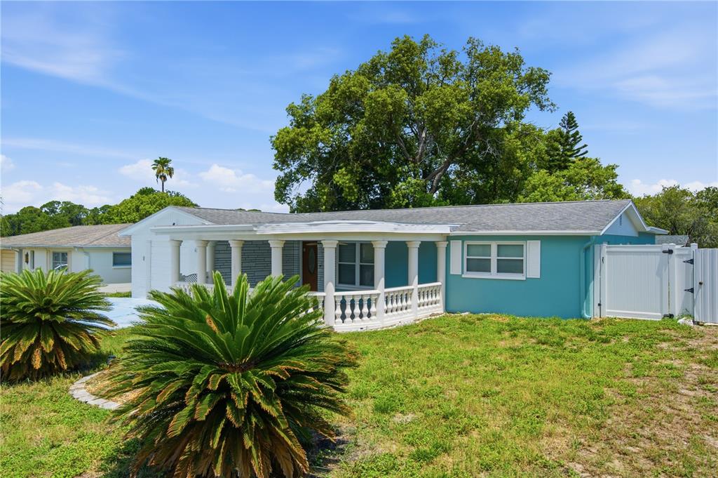 A teal single-story house features a covered front porch with white columns and railings — 6345 PATELLA AVENUE, NEW PORT RICHEY, FL