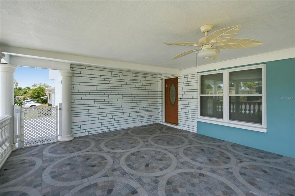 A covered porch features patterned tile flooring, a ceiling fan, and a stone-textured wall — 6345 PATELLA AVENUE, NEW PORT RICHEY, FL