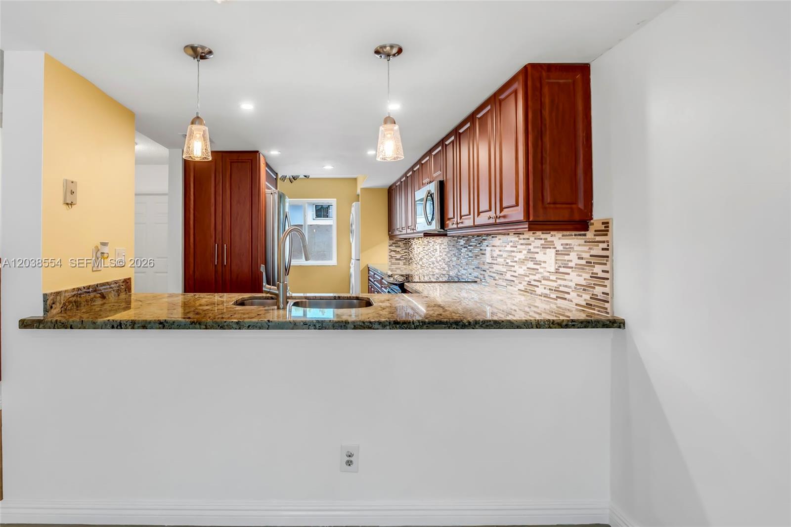 A kitchen features dark wood cabinets, granite countertops, a mosaic backsplash, and two pendant lights — 7050 SW 42nd Ct, Davie FL 33314, DAVIE, FL