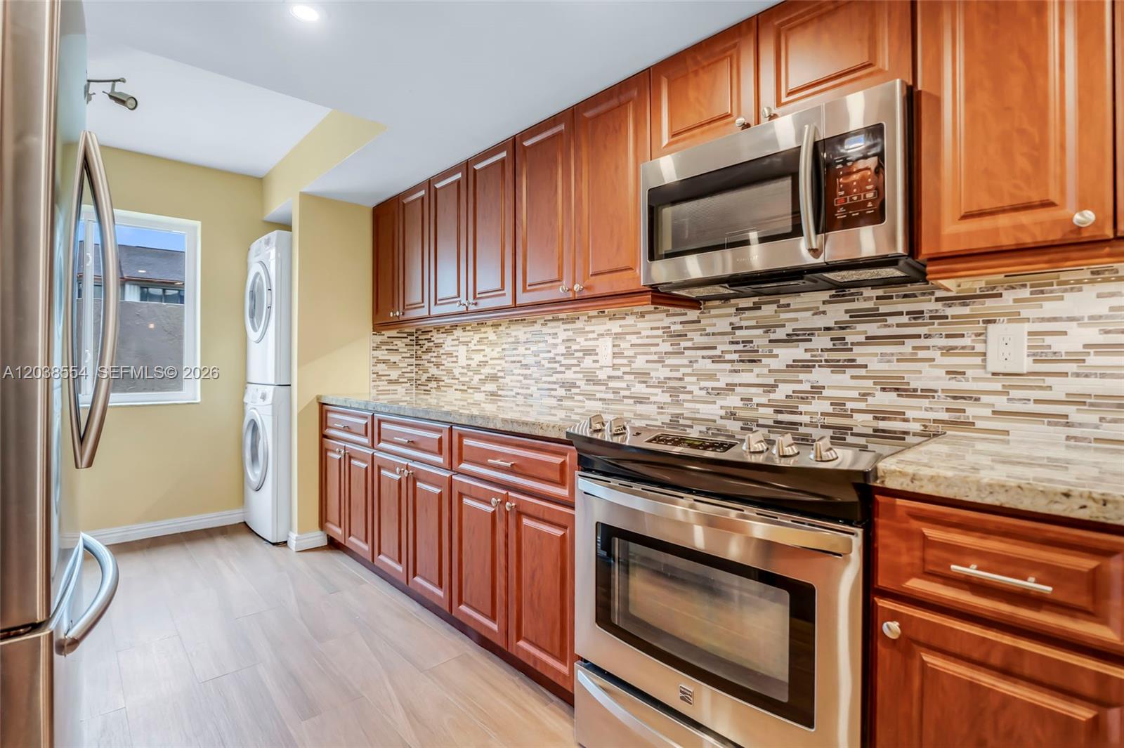 A kitchen features wood cabinets, stainless steel appliances, a tiled backsplash, and a stacked laundry unit — 7050 SW 42nd Ct, Davie FL 33314, DAVIE, FL