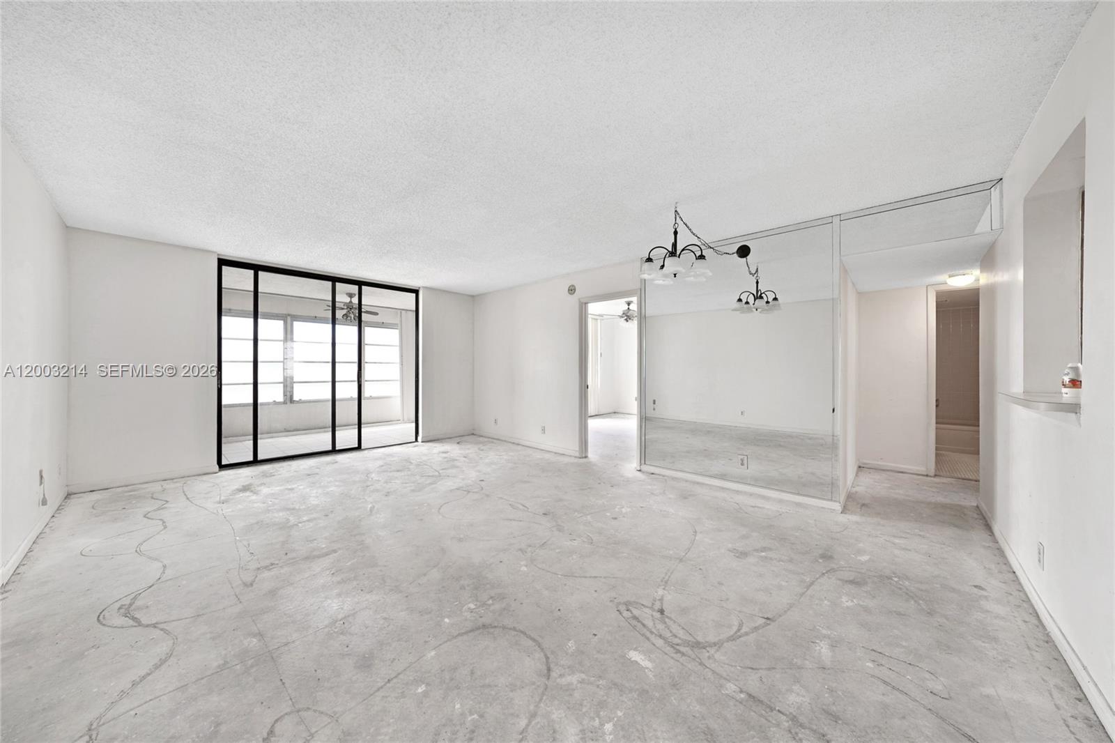 An empty room features concrete flooring, white walls, a mirrored accent wall, and sliding glass doors — 7330 NW 18th St # 204, Margate FL 33063, MARGATE, FL