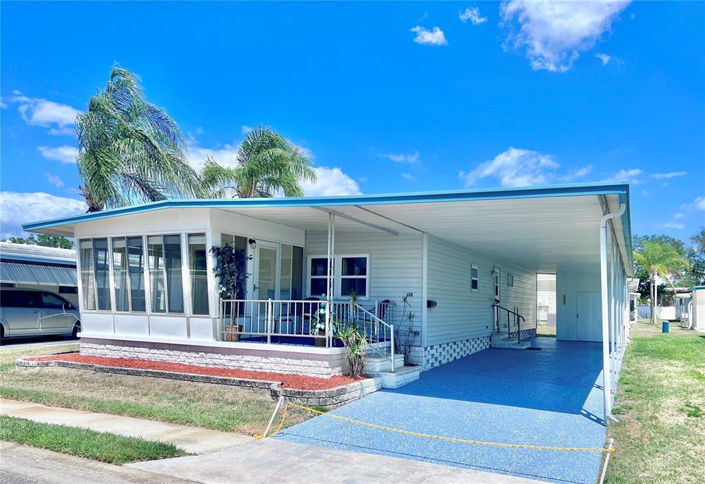 A light-colored mobile home features a screened-in porch, a carport, and a blue driveway — 1100 BELCHER ROAD S UNIT 130, LARGO, FL