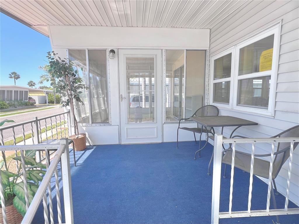 A covered porch features blue carpeting, a small metal table, chairs, and white siding — 1100 BELCHER ROAD S UNIT 130, LARGO, FL