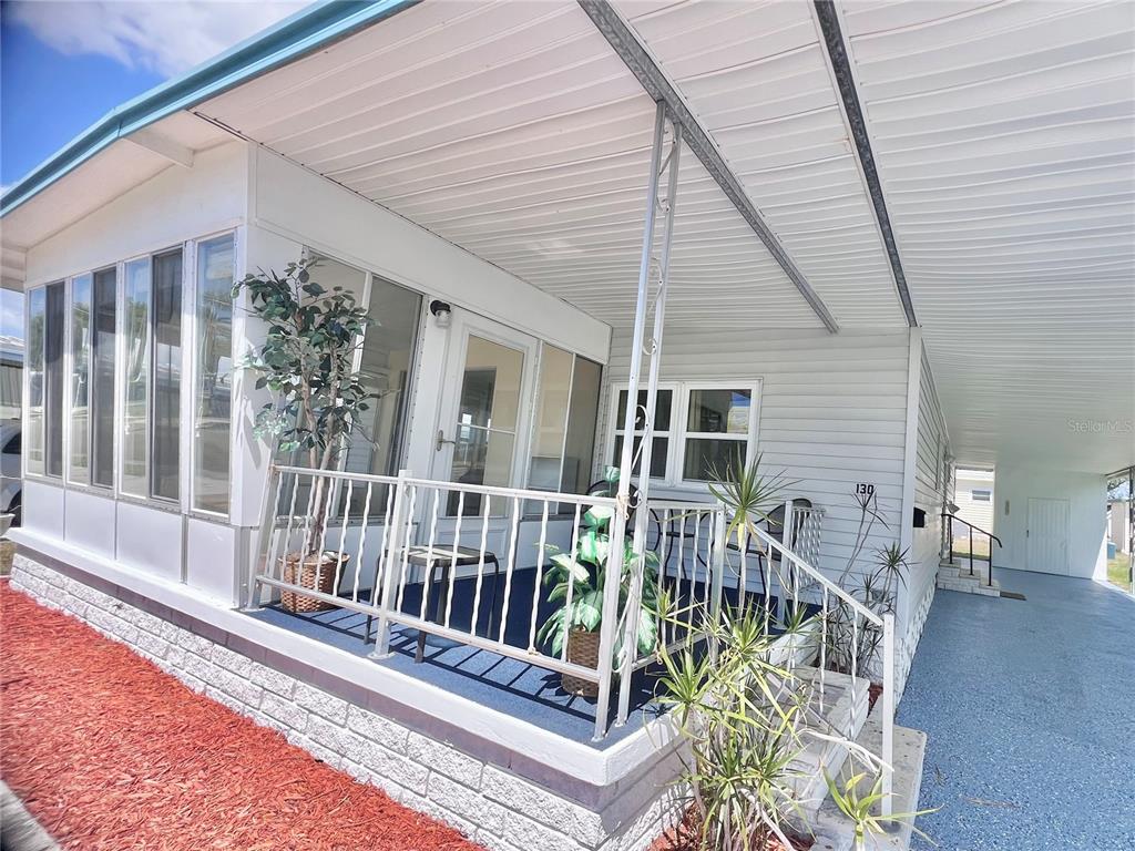 A mobile home features a covered porch with a white railing and a carport — 1100 BELCHER ROAD S UNIT 130, LARGO, FL