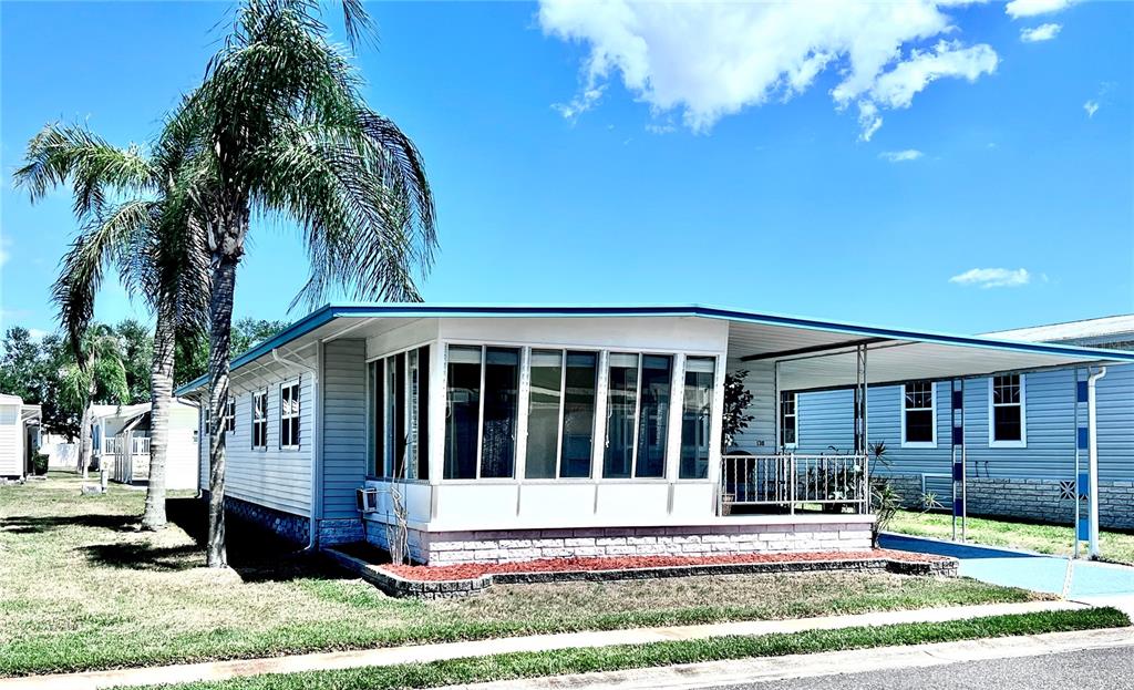 A light-colored manufactured home features a large glass-enclosed porch and an attached carport — 1100 BELCHER ROAD S UNIT 130, LARGO, FL