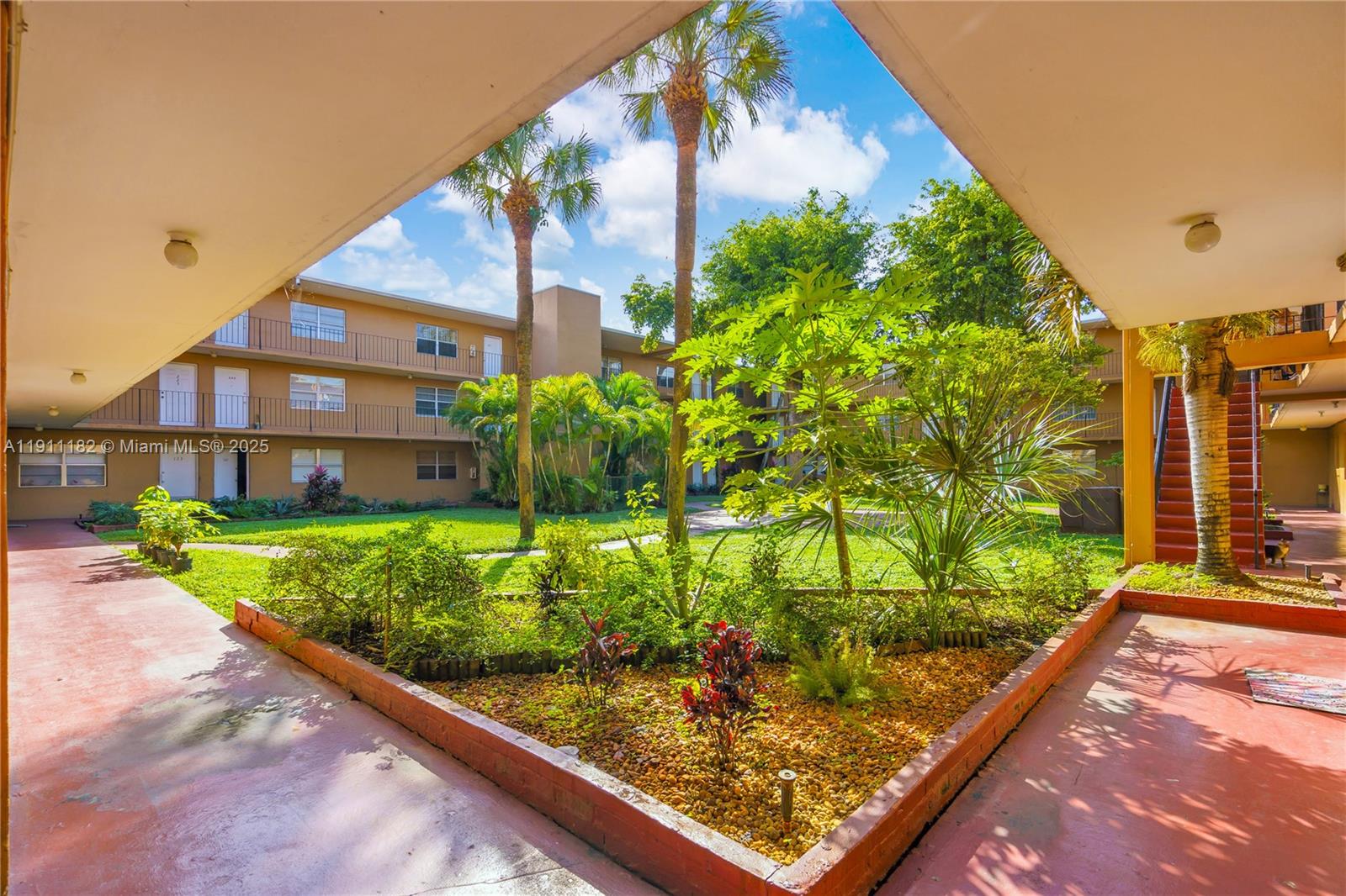 A courtyard with a garden and palm trees is viewed from a covered walkway — 1330 W 54th St # 302C, Hialeah FL 33012, HIALEAH, FL