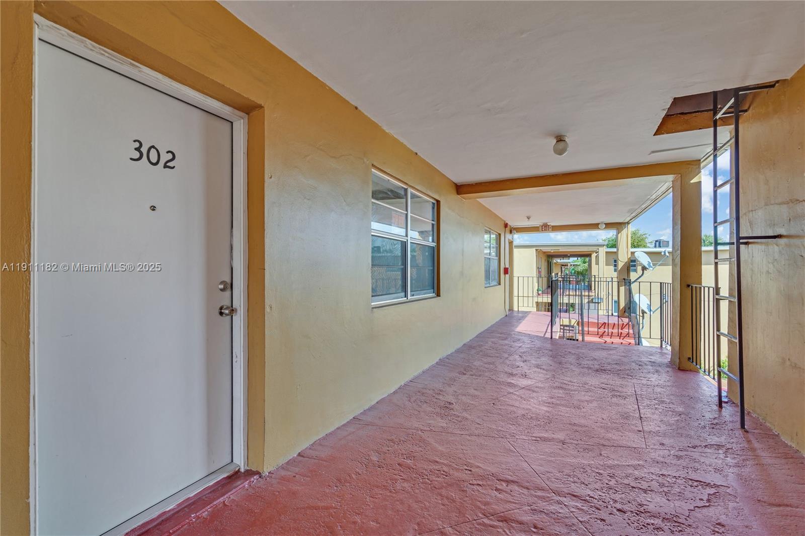 An exterior walkway leads to unit 302, featuring a red painted floor and metal ladder — 1330 W 54th St # 302C, Hialeah FL 33012, HIALEAH, FL