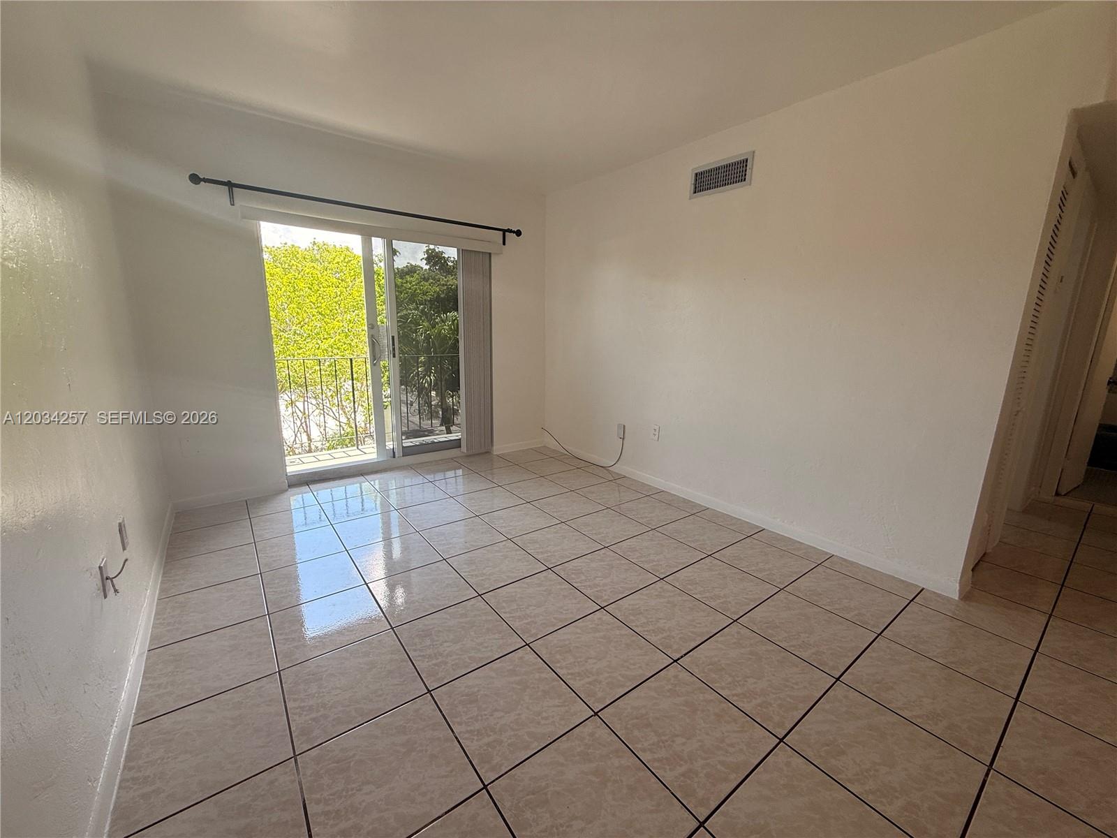 An empty room features beige tile flooring, white walls, and a sliding glass balcony door — 1860 SW 22nd St # 11, Miami FL 33145, MIAMI, FL