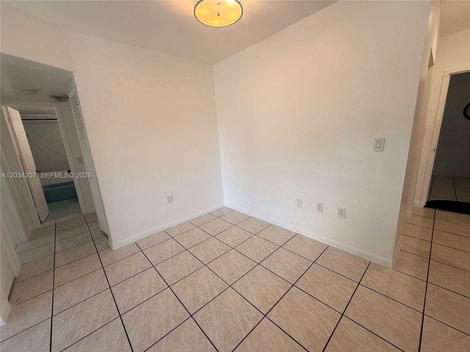 An empty room features white walls, beige tiled flooring, and a central ceiling light fixture — 1860 SW 22nd St # 11, Miami FL 33145, MIAMI, FL