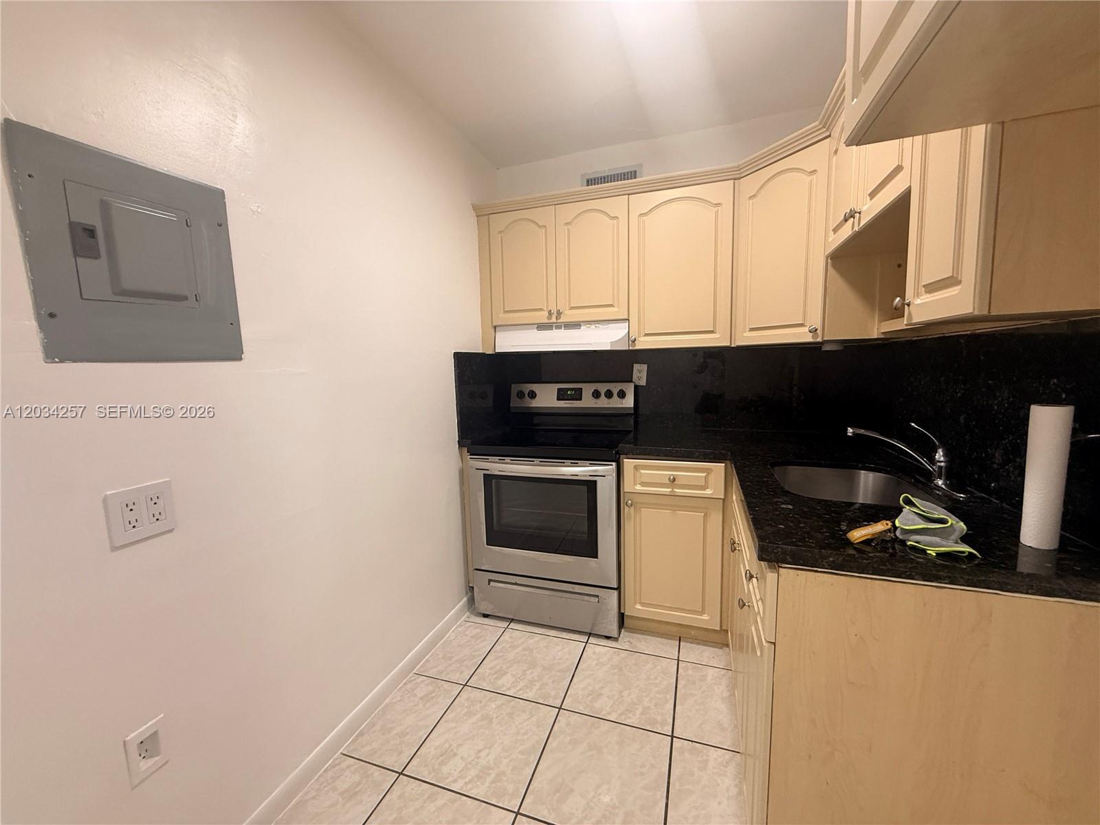 A small kitchen features beige cabinets, black countertops, stainless steel appliances, and tiled flooring — 1860 SW 22nd St # 11, Miami FL 33145, MIAMI, FL