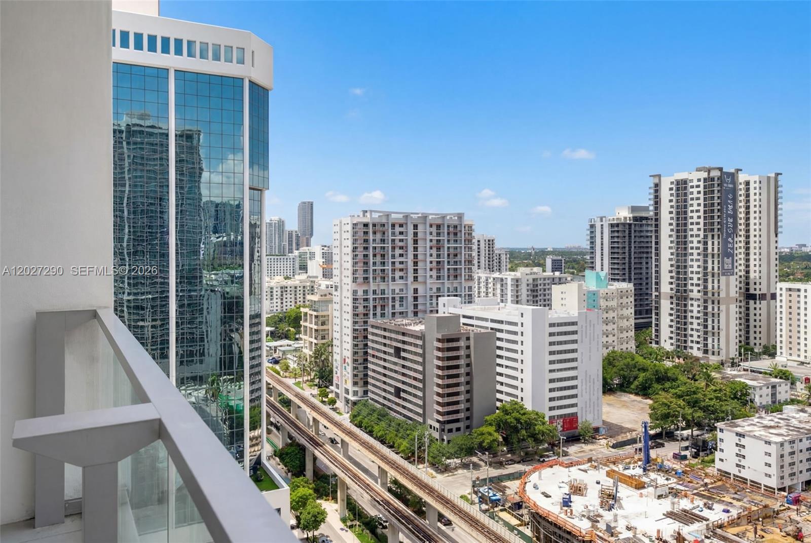 A high-angle view from a balcony overlooks a city skyline with buildings and a train track — 88 SW 7th St # 2408, Miami FL 33130, MIAMI, FL