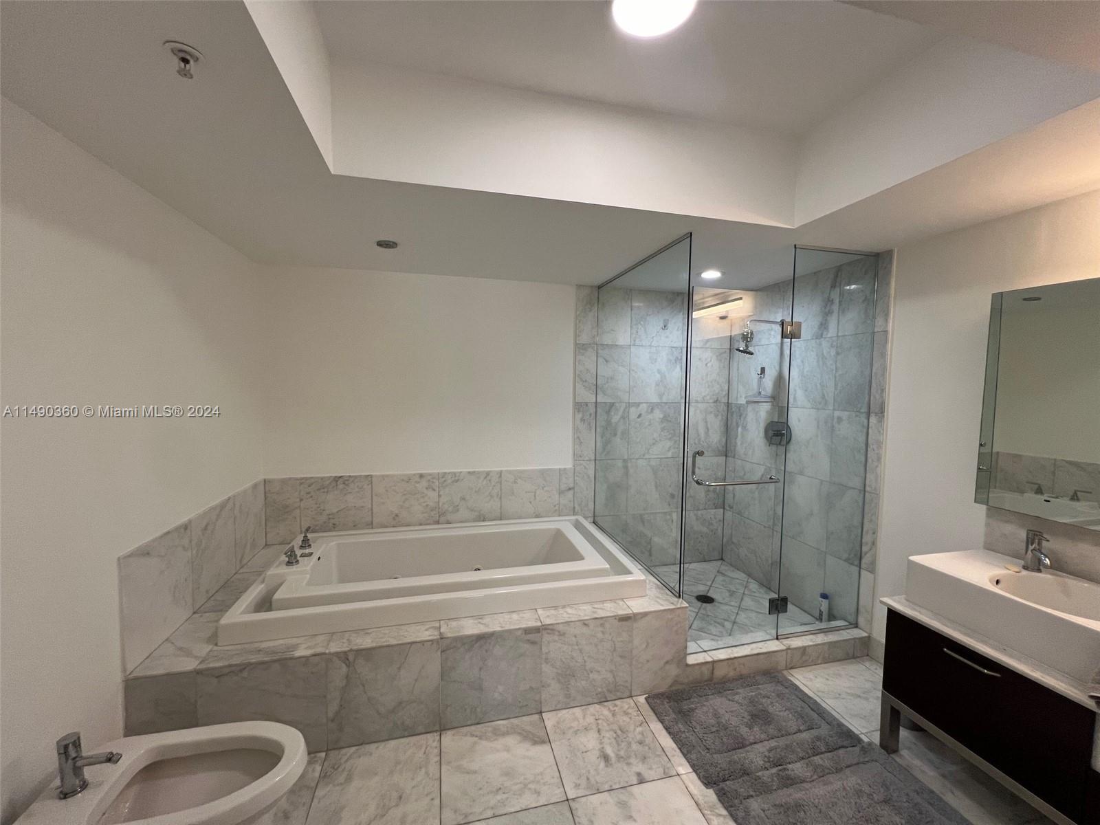 A bathroom features a marble-tiled soaking tub, a glass-enclosed shower, and a modern vanity — 218 SE 14th Street # 1806, Miami FL 33131, MIAMI, FL