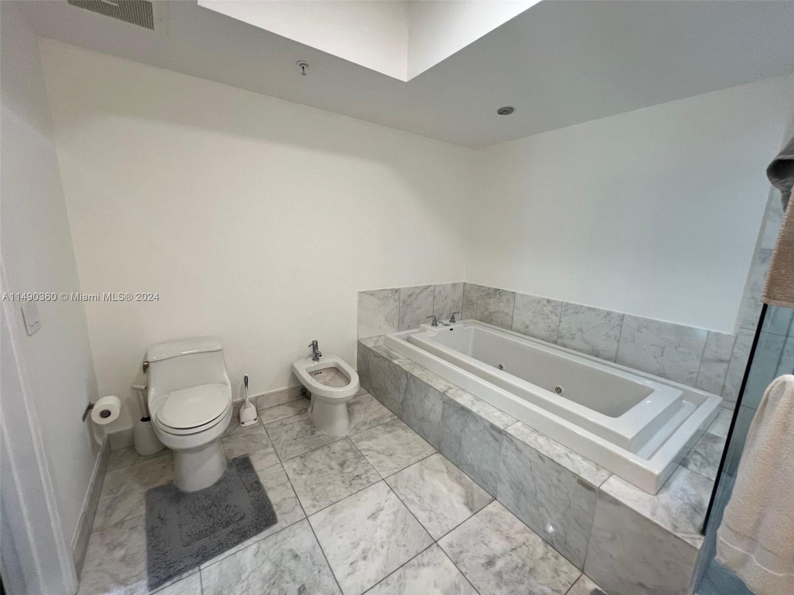A bathroom features a white toilet, a bidet, and a marble-tiled soaking tub — 218 SE 14th Street # 1806, Miami FL 33131, MIAMI, FL