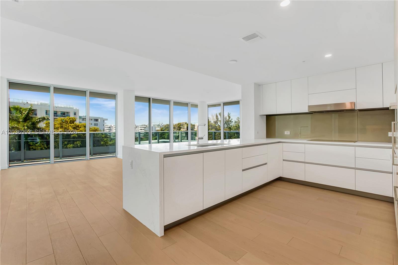 A modern kitchen features white cabinetry, a large island, and floor-to-ceiling windows with balcony views — 9221 E Bay Harbor Drive # 512, Bay Harbor Islands FL 33154, BAY HARBOR ISLANDS, FL