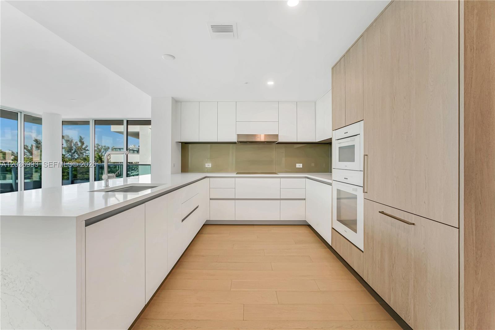 A modern kitchen features white cabinetry, light wood paneling, and a white quartz island — 9221 E Bay Harbor Drive # 512, Bay Harbor Islands FL 33154, BAY HARBOR ISLANDS, FL