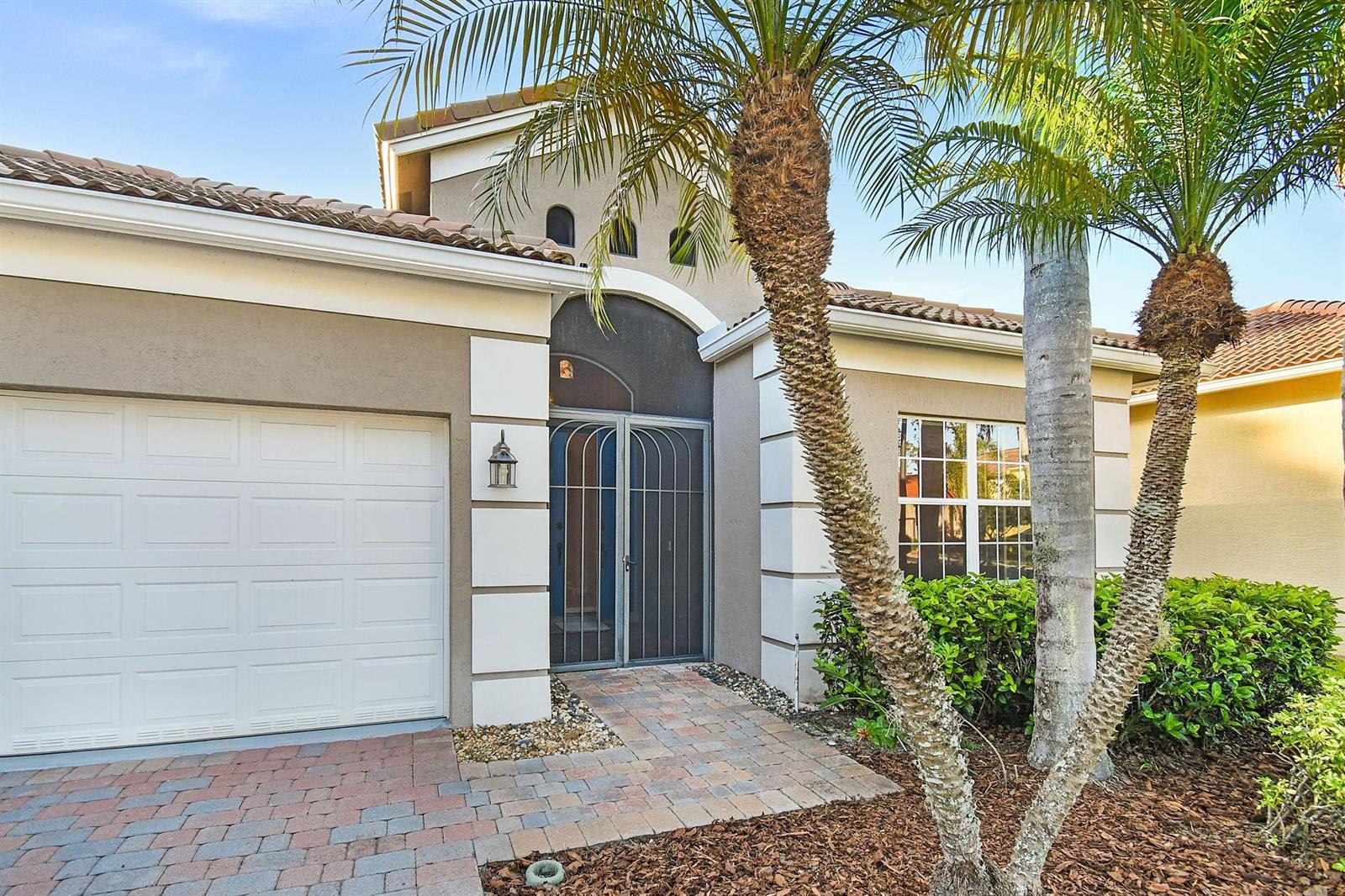 The exterior of a house features a white garage door, a screened entryway, and palm trees — 7084 SE Cricket Court, Stuart FL 34997, STUART, FL