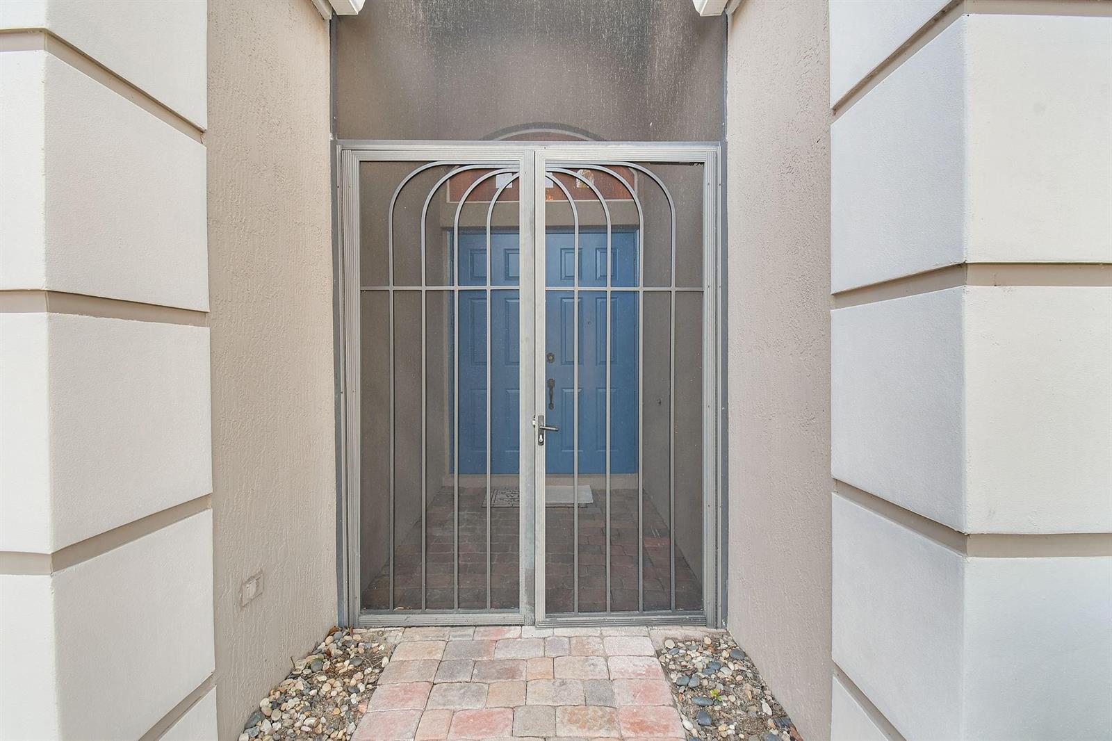 A metal security screen door stands in front of a blue double door entrance — 7084 SE Cricket Court, Stuart FL 34997, STUART, FL
