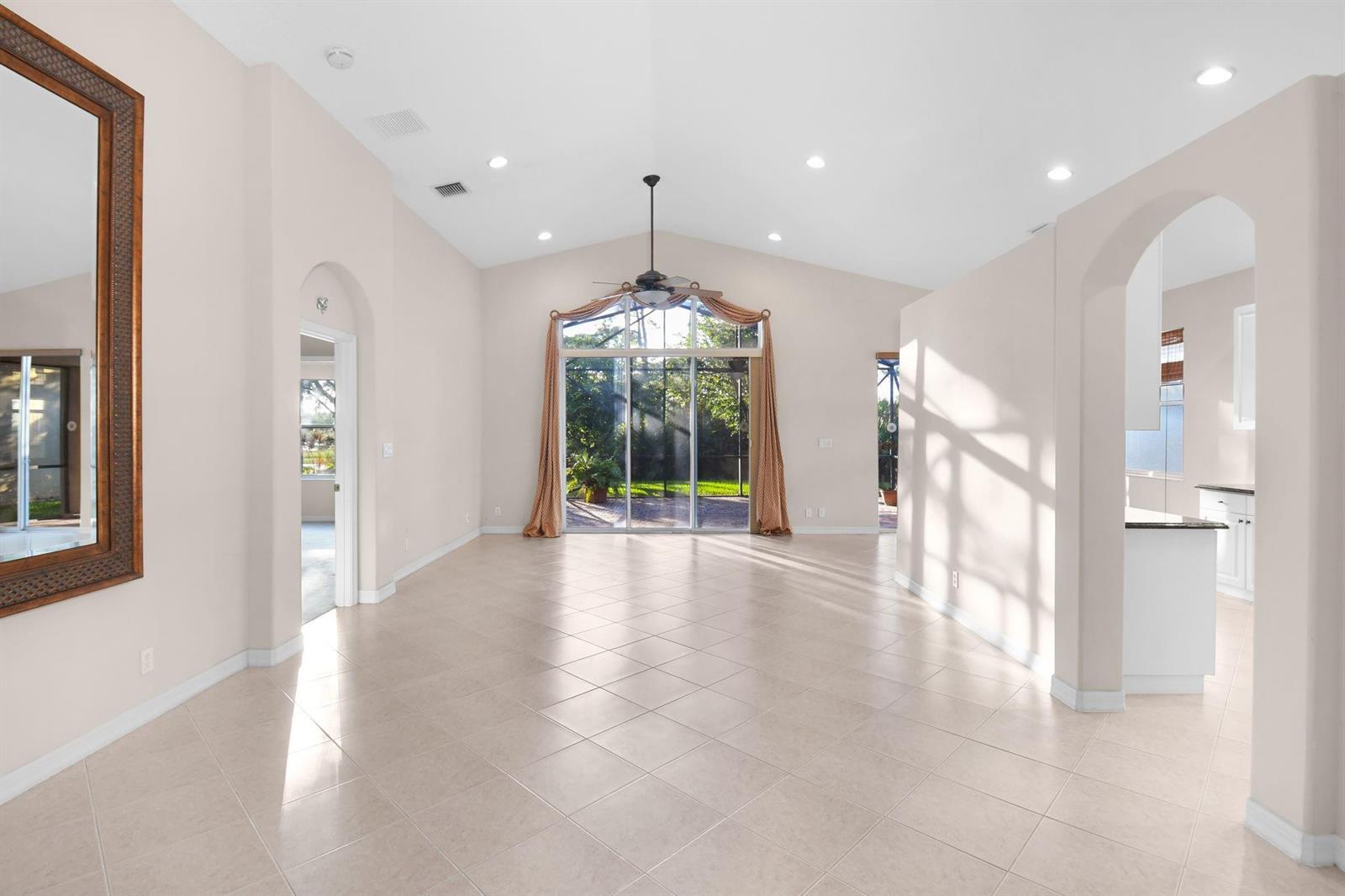A spacious living room with vaulted ceilings, tile flooring, and large sliding glass doors — 7084 SE Cricket Court, Stuart FL 34997, STUART, FL
