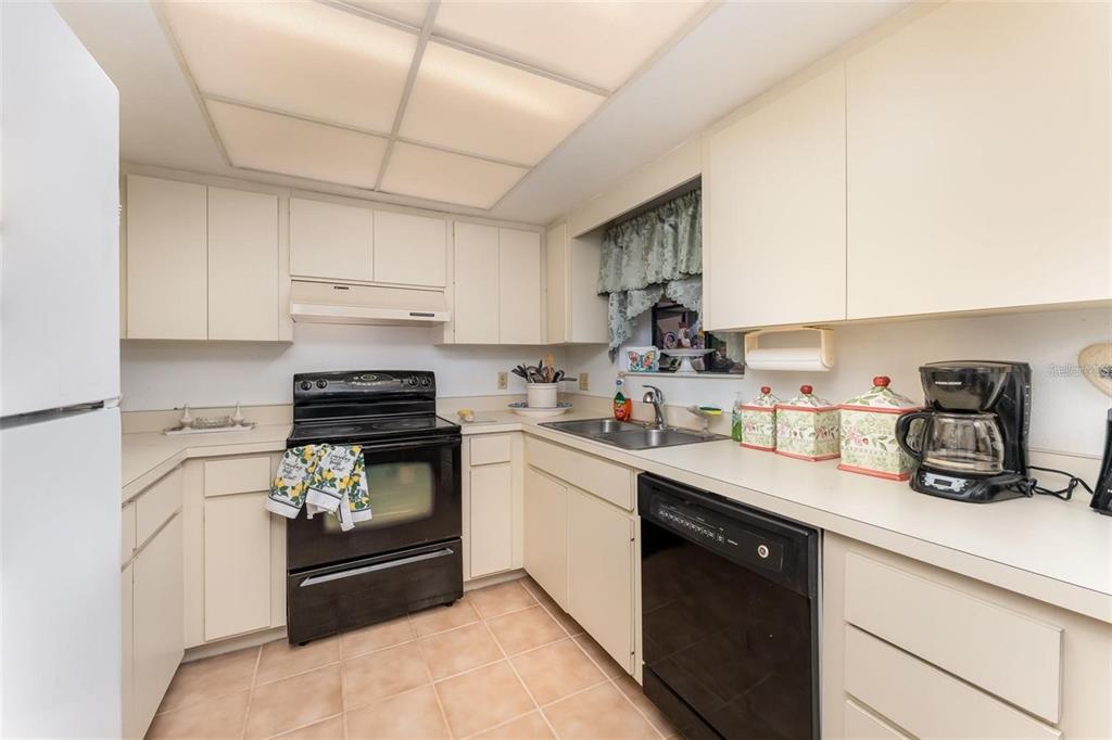 A kitchen features off-white cabinets, black appliances, a tiled floor, and a drop ceiling — 6314 29TH AVENUE W, BRADENTON, FL