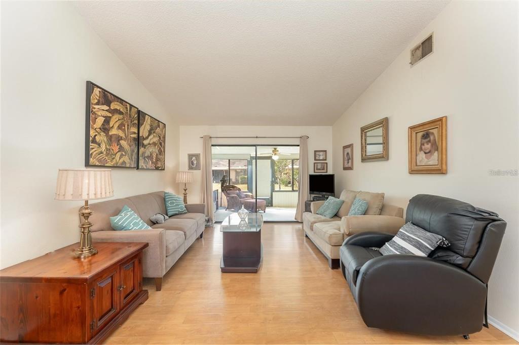 A living room features light wood flooring, two sofas, a black recliner, and sliding glass doors — 6314 29TH AVENUE W, BRADENTON, FL