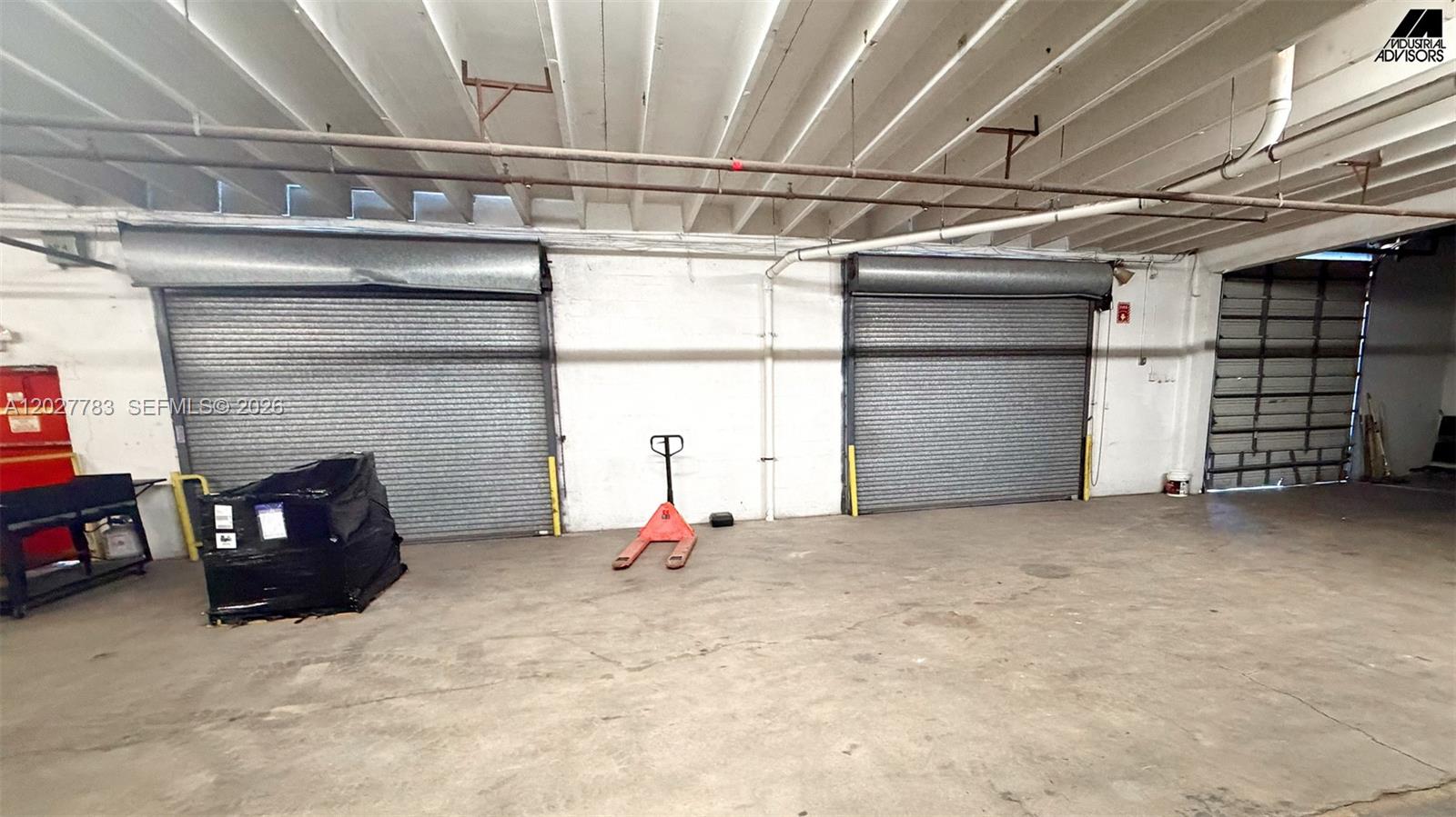 An industrial warehouse interior features concrete floors, exposed ceiling joists, and two metal roll-up doors — 160 Ali Baba Ave, Opa-Locka FL 33054, OPA-LOCKA, FL