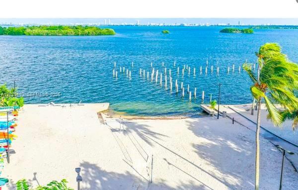 A sandy beach area features a wooden dock extending into a calm blue bay — 750 NE 64th St # B316, Miami FL 33138, MIAMI, FL