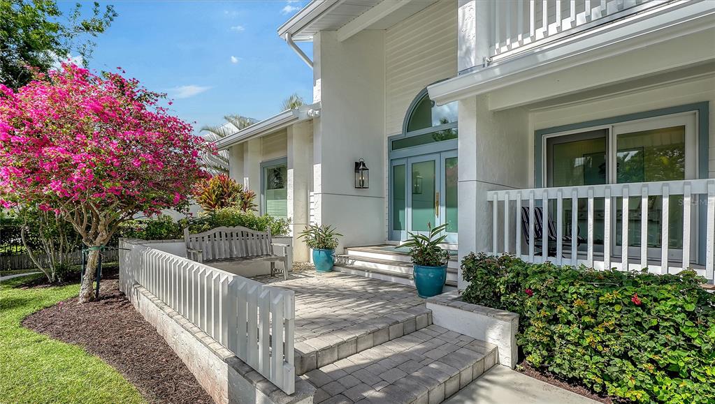 A white house exterior features a paved patio, a wooden bench, and vibrant pink landscaping — 476 MEADOW LARK DRIVE, SARASOTA, FL