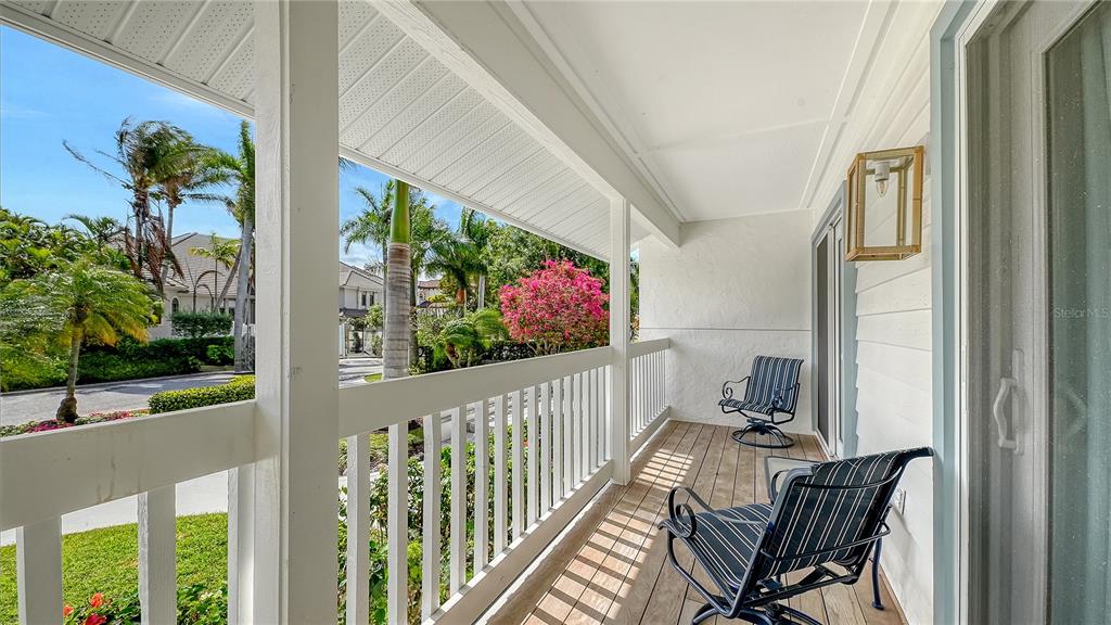 A covered balcony features white railings, wood-look flooring, two outdoor chairs, and a view of palm trees — 476 MEADOW LARK DRIVE, SARASOTA, FL