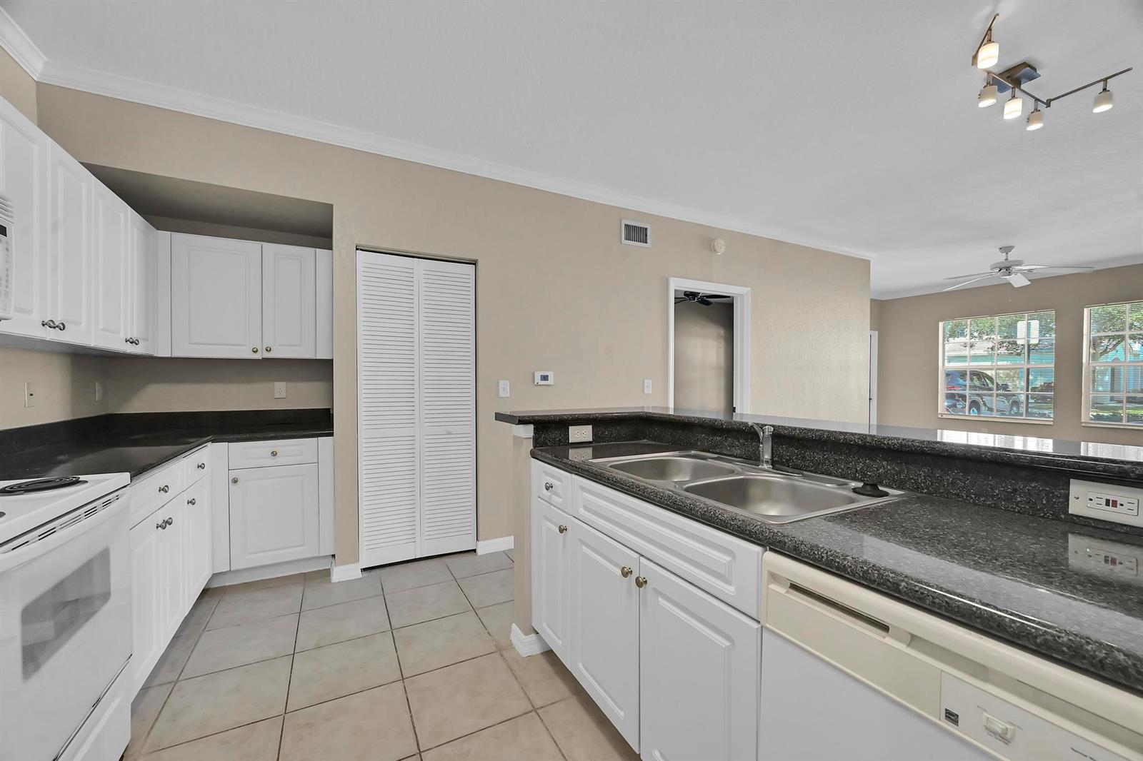 A kitchen features white cabinets, dark granite countertops, tile flooring, and an open-concept living area — 196 SE Kitching Circle, Stuart FL 34994, STUART, FL