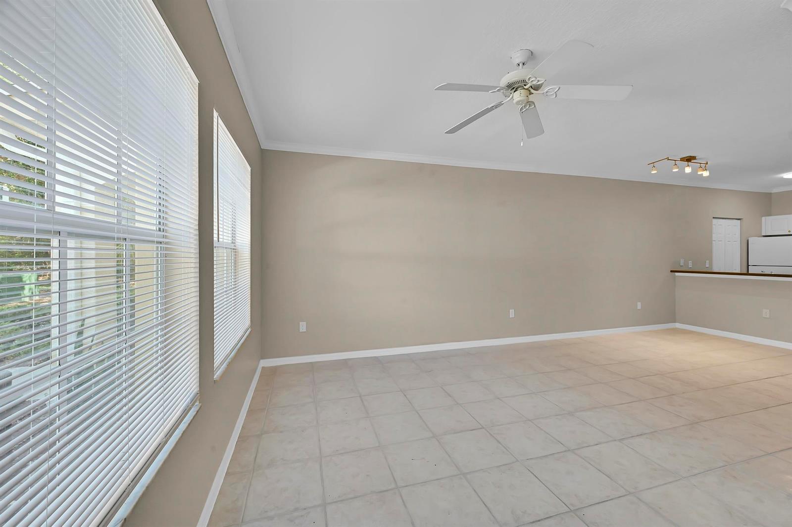 An empty living room features beige walls, white tile flooring, a ceiling fan, and blinds — 196 SE Kitching Circle, Stuart FL 34994, STUART, FL