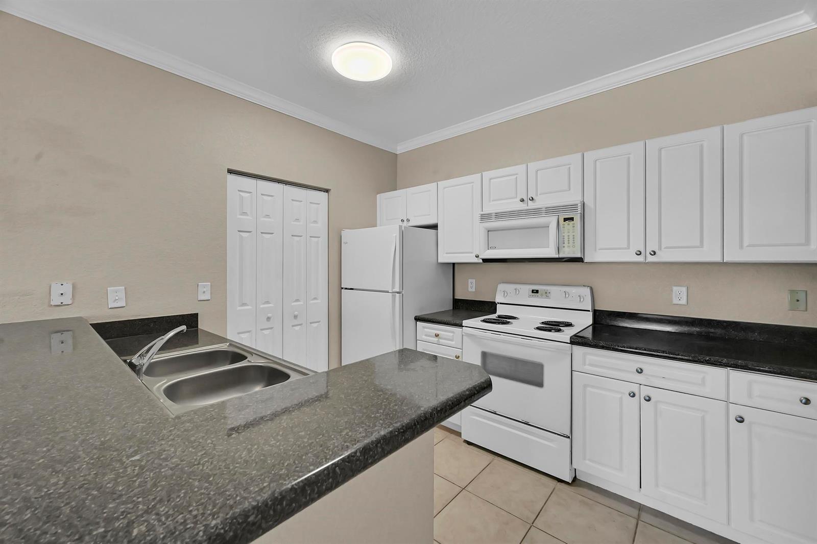 A kitchen features white cabinets, black countertops, white appliances, and a breakfast bar — 196 SE Kitching Circle, Stuart FL 34994, STUART, FL