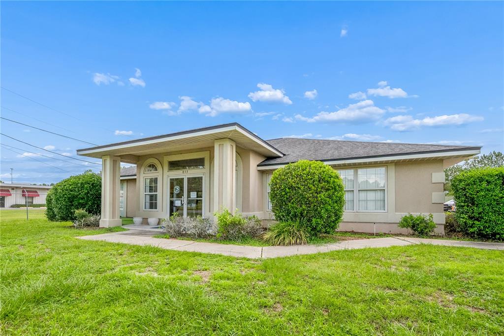 A single-story commercial building with a covered entrance, beige stucco walls, and manicured landscaping — 853 SW SISTERS WELCOME ROAD, LAKE CITY, FL