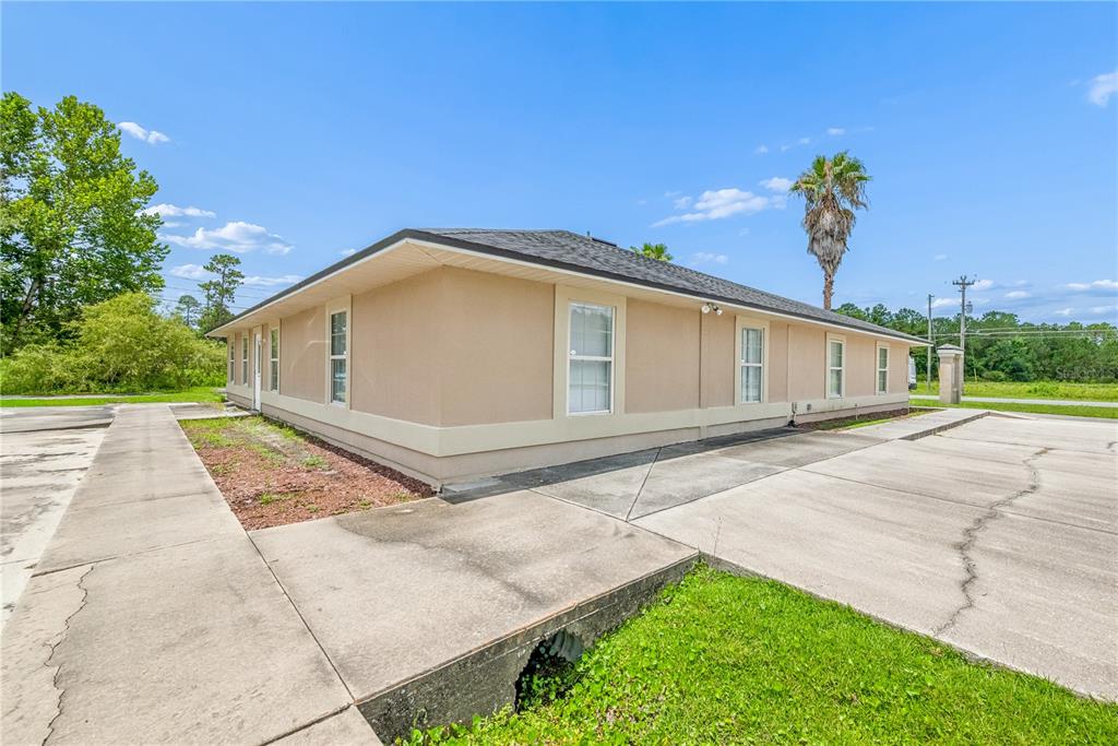 A beige, single-story commercial building with a hip roof and concrete parking area — 853 SW SISTERS WELCOME ROAD, LAKE CITY, FL