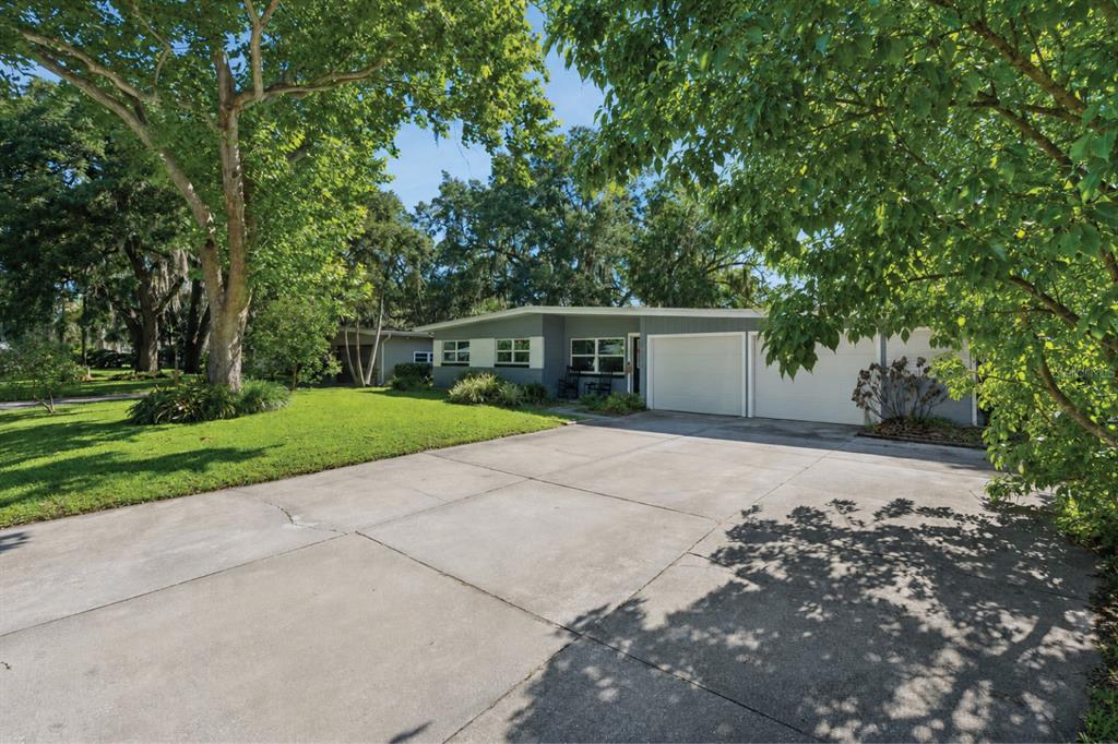 A gray single-story house features a two-car garage, a concrete driveway, and mature shade trees — 4533 STILWELL DRIVE, ORLANDO, FL