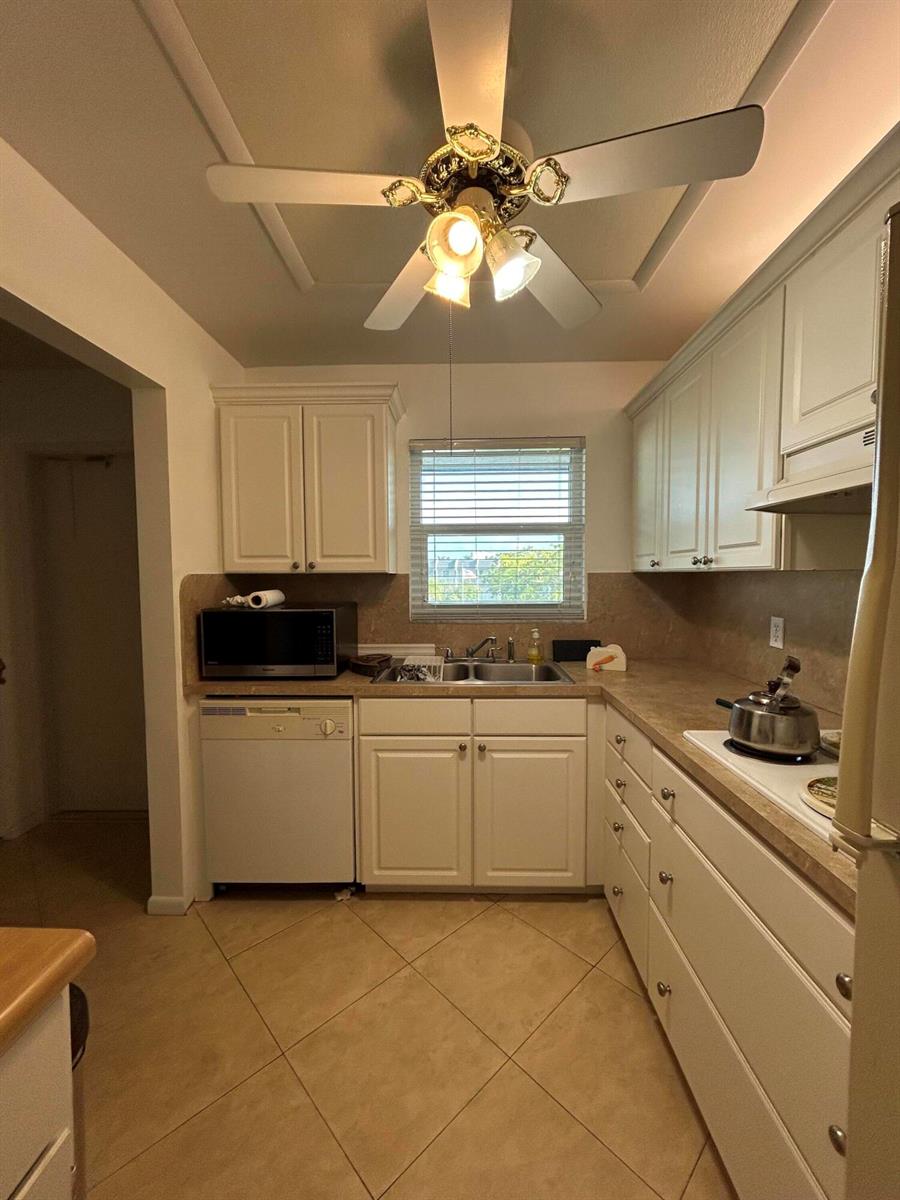 A kitchen features white cabinets, tan countertops, tile flooring, and a ceiling fan — 6600 Royal Palm Boulevard # 304b, Margate FL 33063, MARGATE, FL
