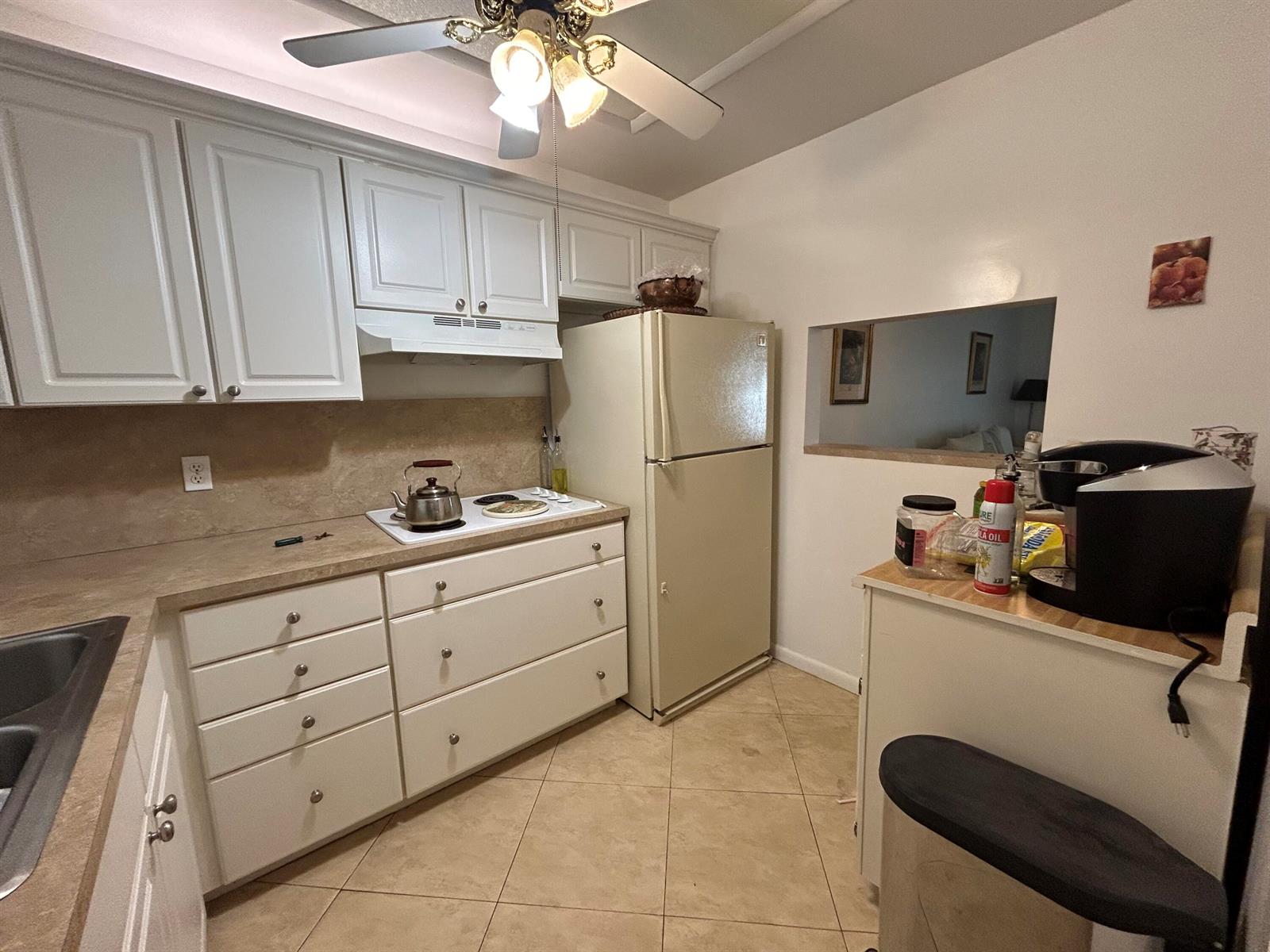 A kitchen features white cabinetry, a beige refrigerator, a stove, and tile flooring — 6600 Royal Palm Boulevard # 304b, Margate FL 33063, MARGATE, FL