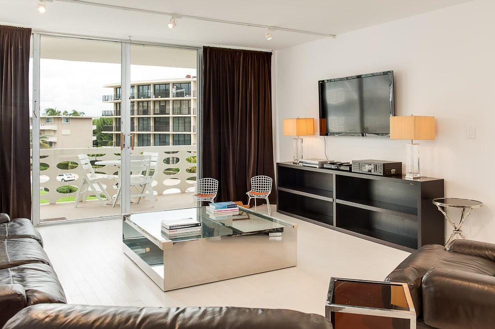 A modern living room features a mirrored coffee table, dark leather sofas, and a balcony view — 100 Sunrise Avenue # 404, Palm Beach FL 33480, PALM BEACH, FL