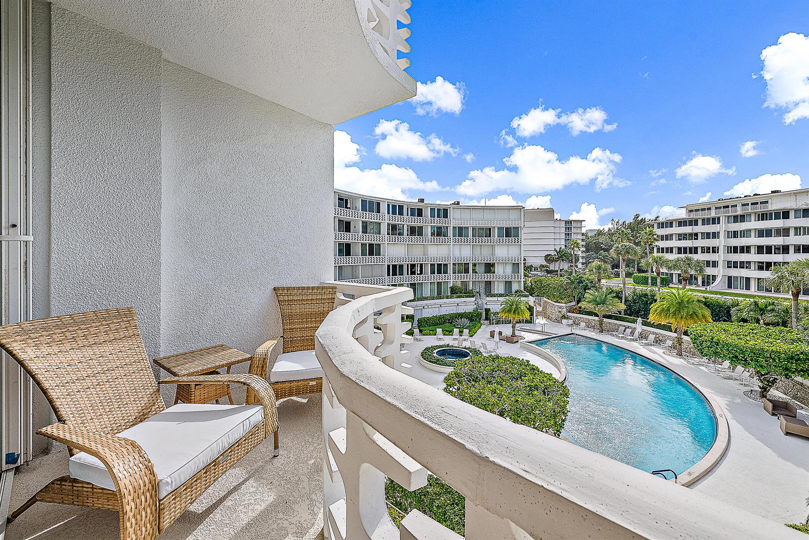 A balcony with wicker chairs overlooks a swimming pool and multi-story residential buildings — 2760 S Ocean Boulevard # 310, Palm Beach FL 33480, PALM BEACH, FL