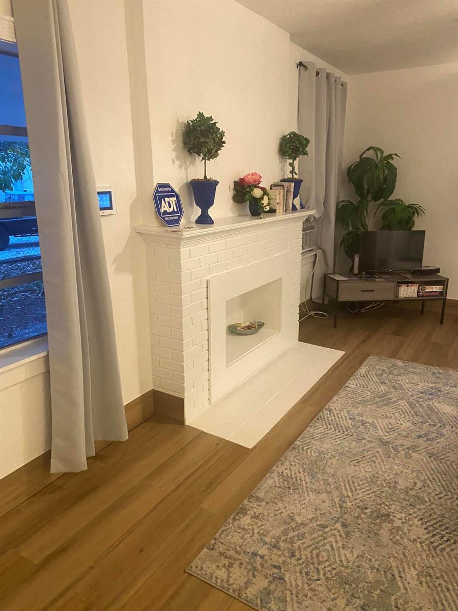 A living room features a white brick fireplace, wood-look flooring, and a patterned area rug — 631 46th Street, West Palm Beach FL 33407, WEST PALM BEACH, FL