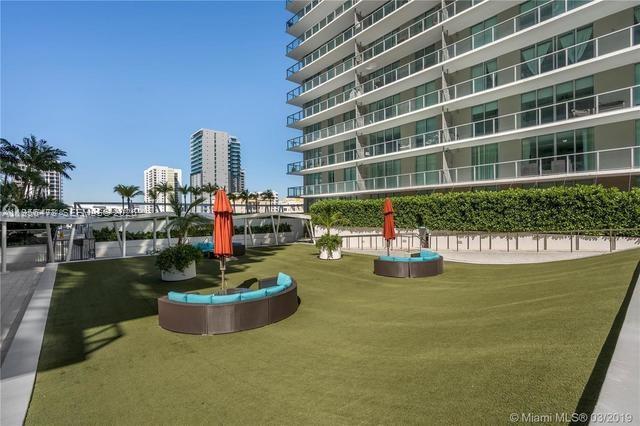 An outdoor terrace features artificial turf, curved lounge seating, and umbrellas beside a tall building — 1111 SW 1st Ave, Miami FL 33130, MIAMI, FL