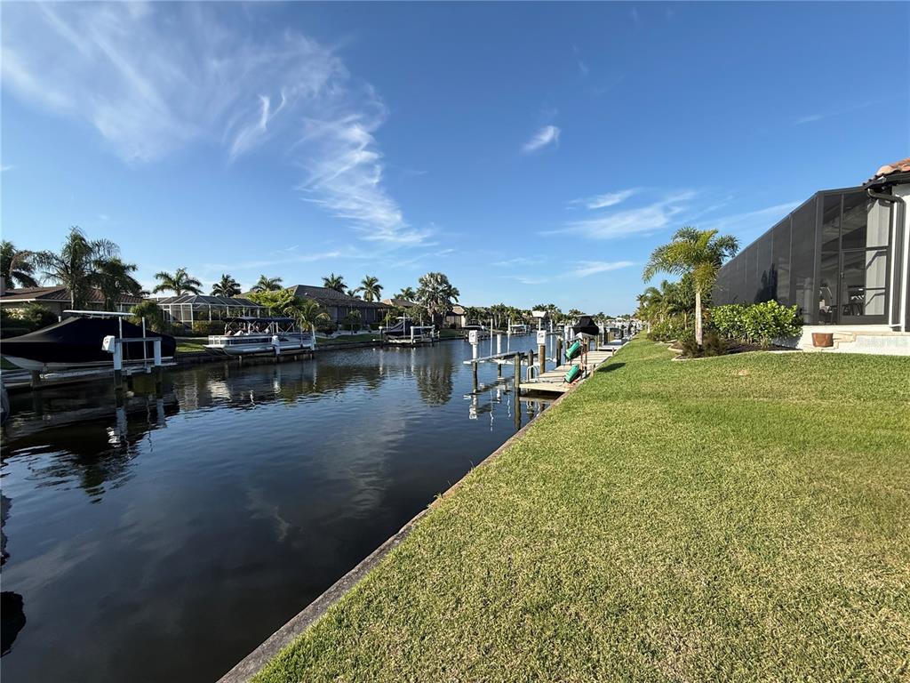 A canal view showing boat docks, a grassy lawn, and a screened-in patio area — 760 ANTALYA COURT, PUNTA GORDA, FL