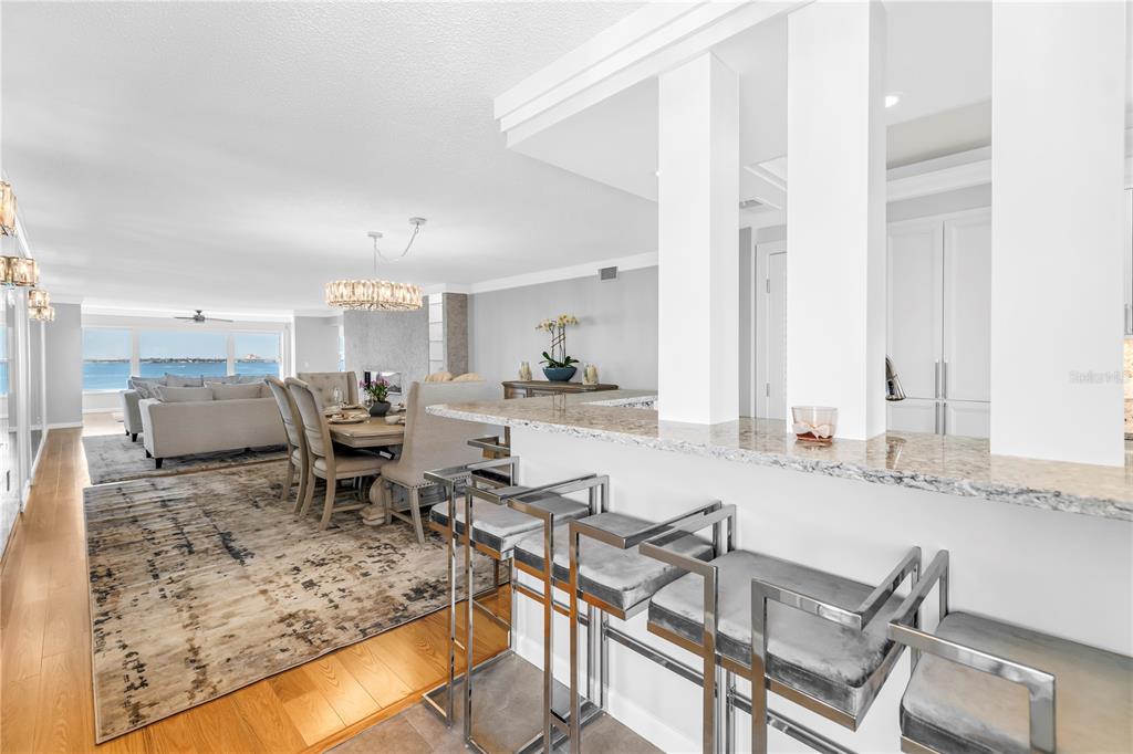 A kitchen breakfast bar with metal stools overlooks a dining area and living room with water views — 6020 SHORE BOULEVARD S UNIT 712, GULFPORT, FL